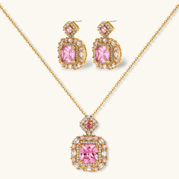 Ornate gold-plated jewelry set with rose pink zirconia center stones and crystal accents on cream background.